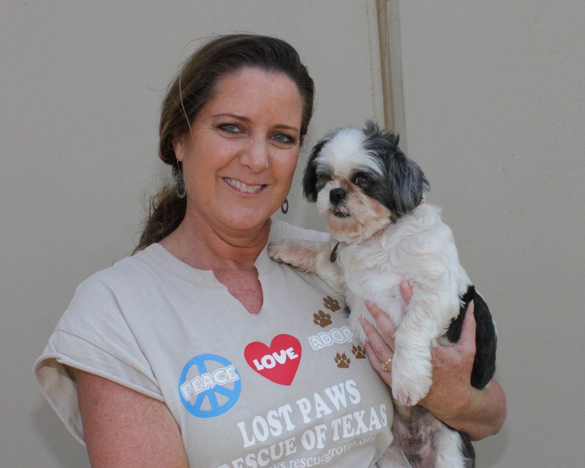 Woman holding a small, black and white dog; she is wearing a shirt that says 