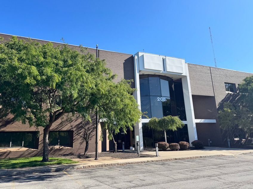 Brick building with a white accent facade; trees in front; blue sky.