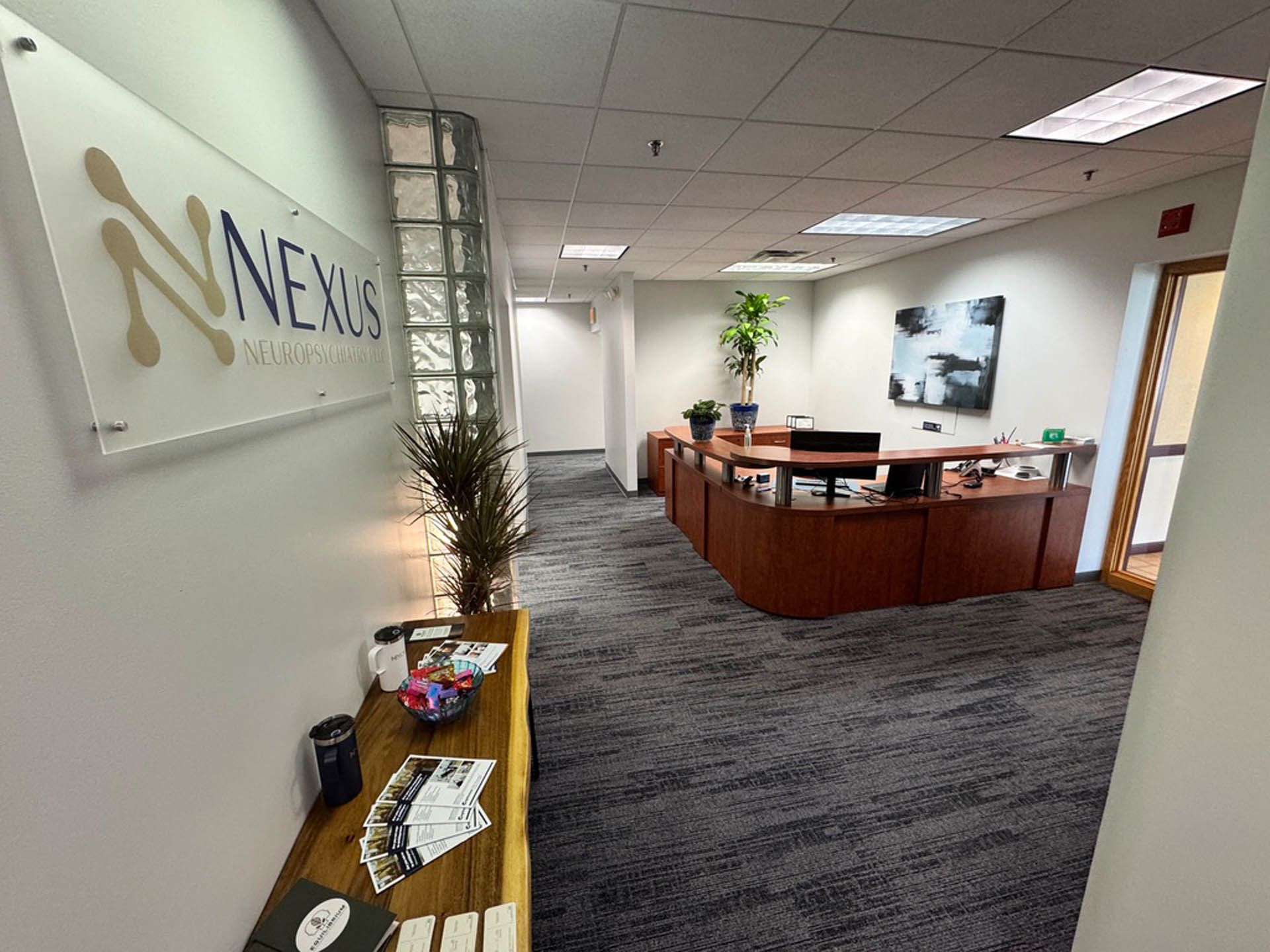 Office entrance with Nexus logo, reception desk, and hallway with gray carpet and white walls.