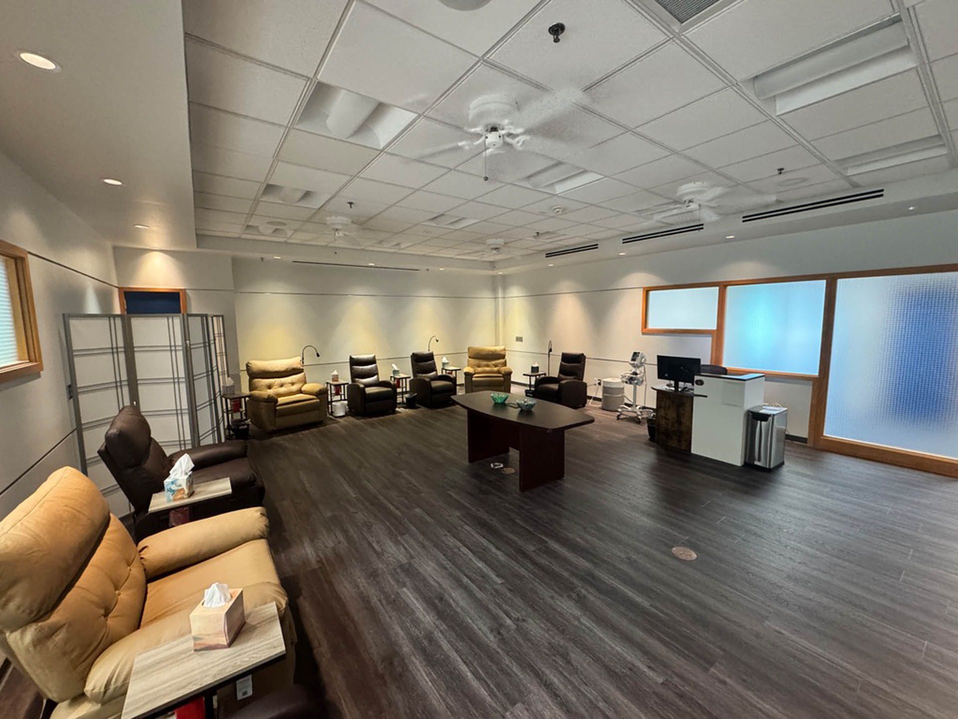 Room with recliners, small tables, and a central coffee table. Windows and screens separate areas.
