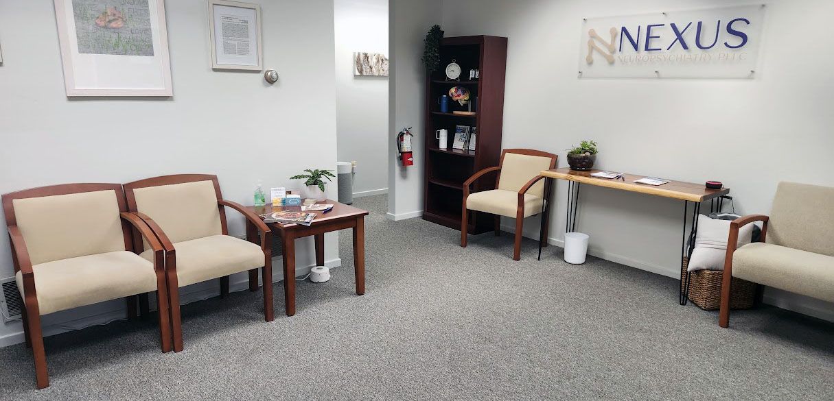 Quiet waiting room with beige chairs, small tables, and a “Nexus” sign on the wall.