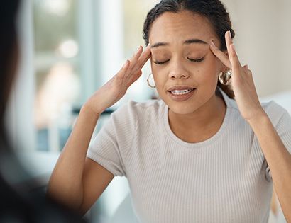 A woman is holding her head in pain while looking at herself in the mirror.