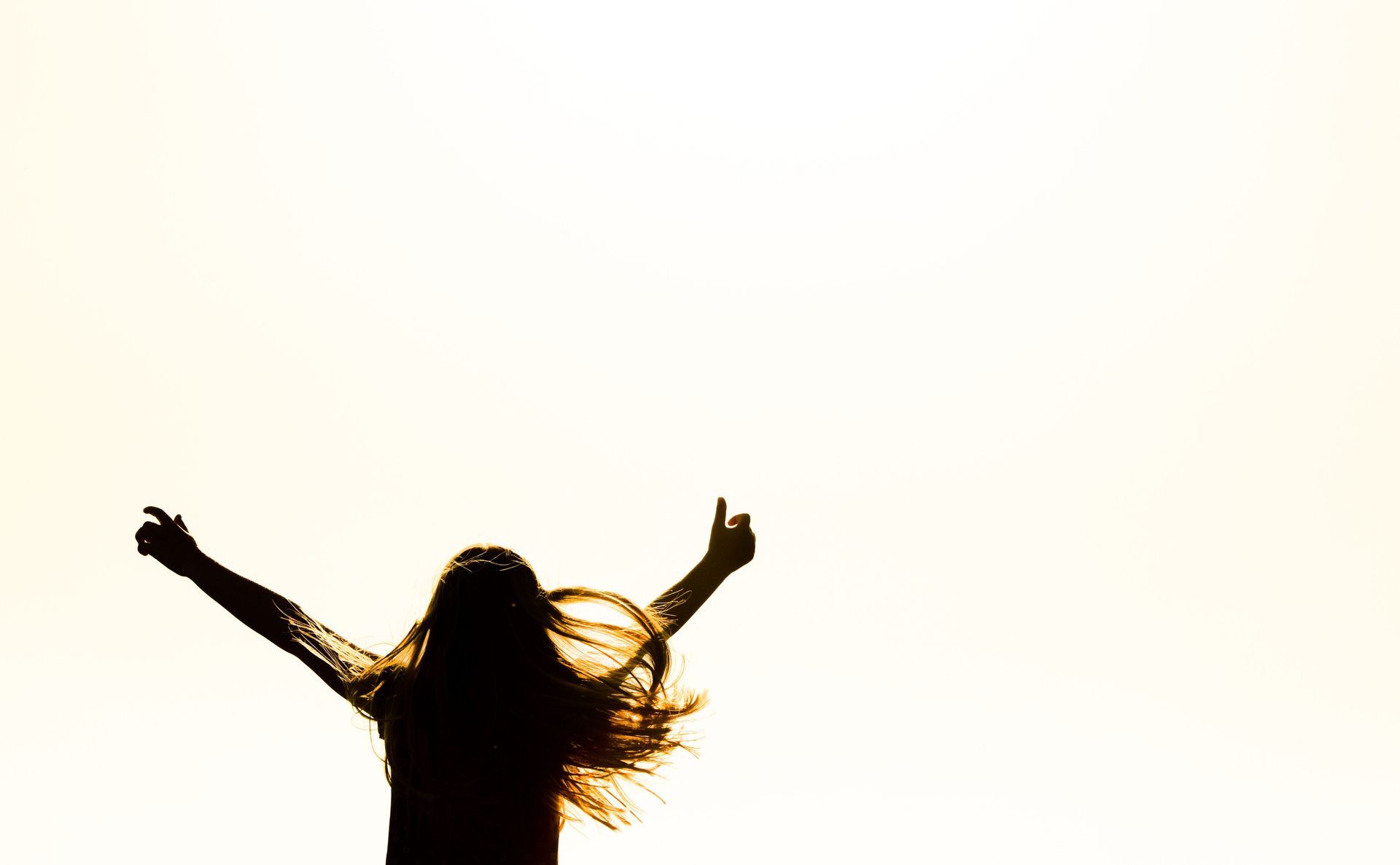 Silhouette of a person with arms raised against a bright white sky