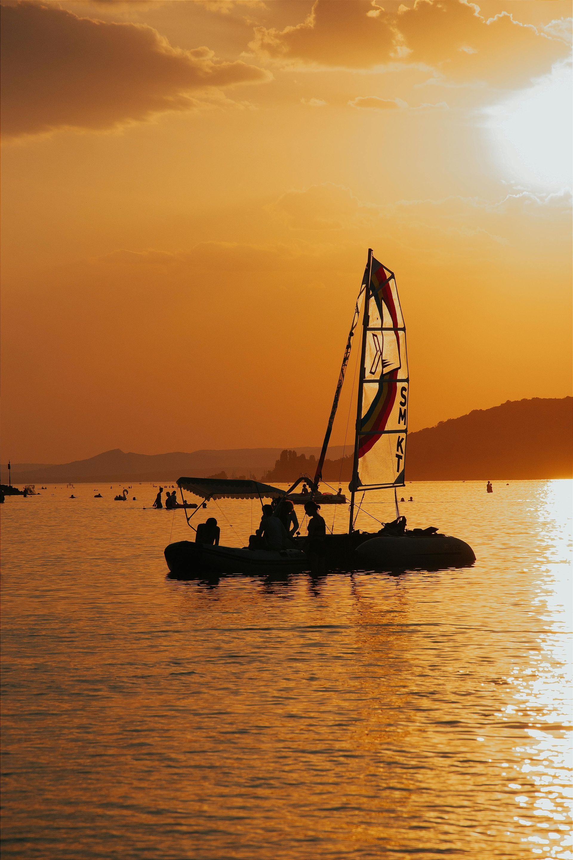 A sailboat is floating on top of a body of water at sunset.