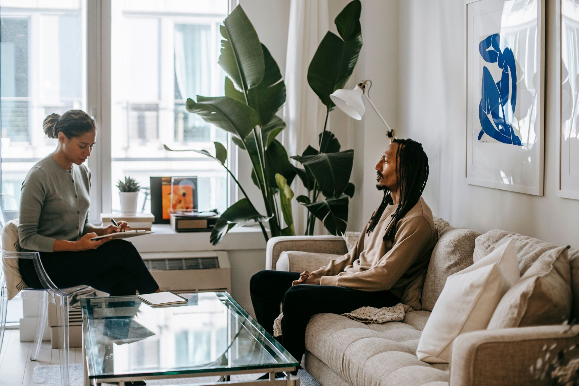 Two people meeting in a bright living room with a laptop and glass coffee table