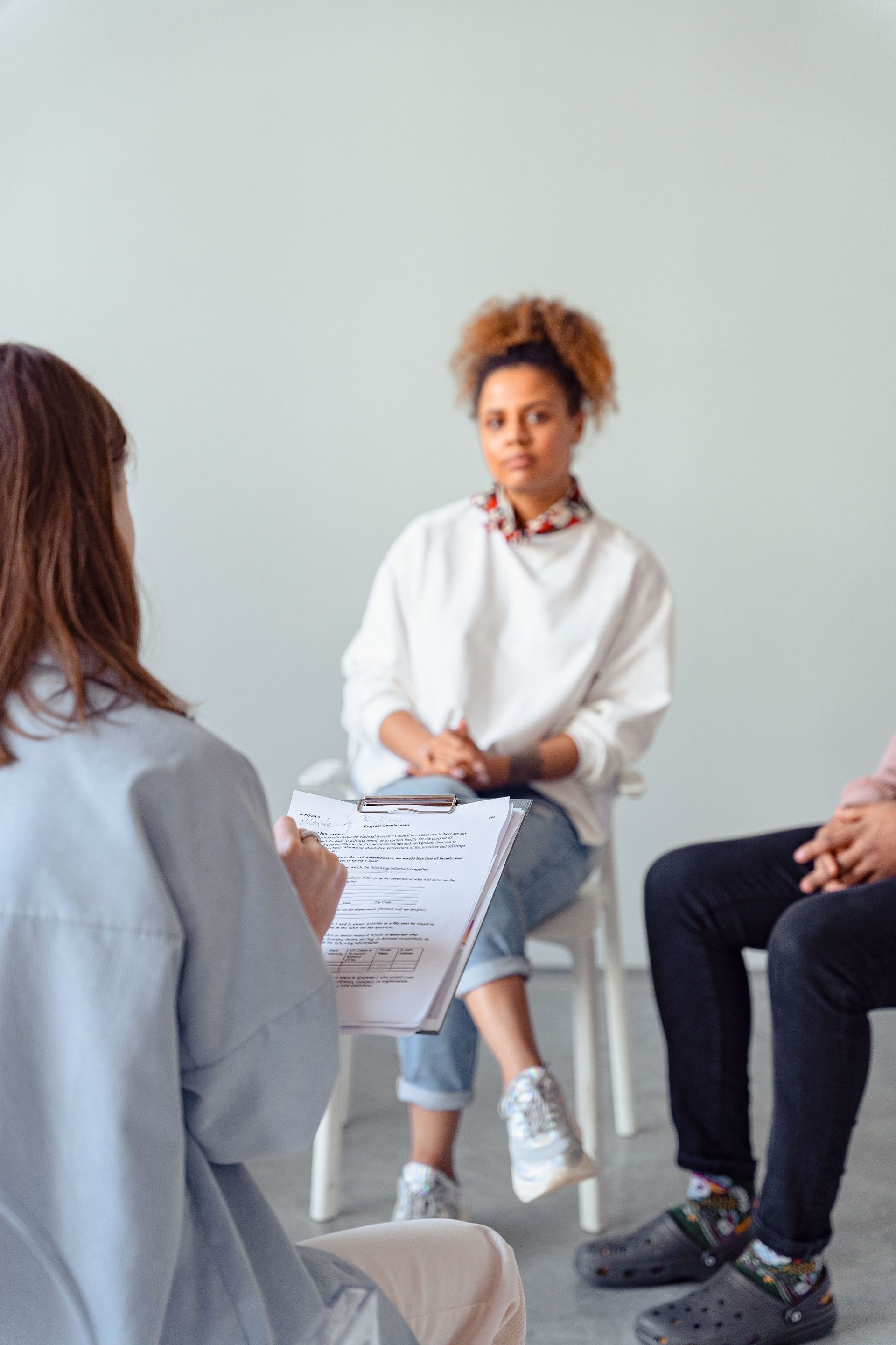 Three people seated in a therapy discussion, with one person speaking and holding a paper.