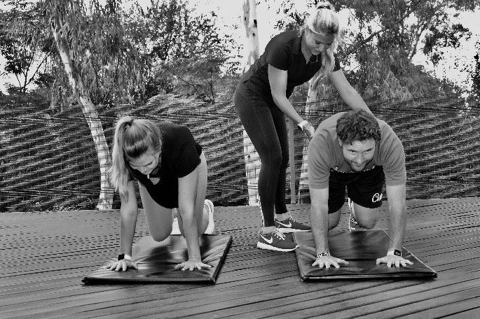 Two people in athletic gear doing an exercise with a trainer on a mat outdoors.