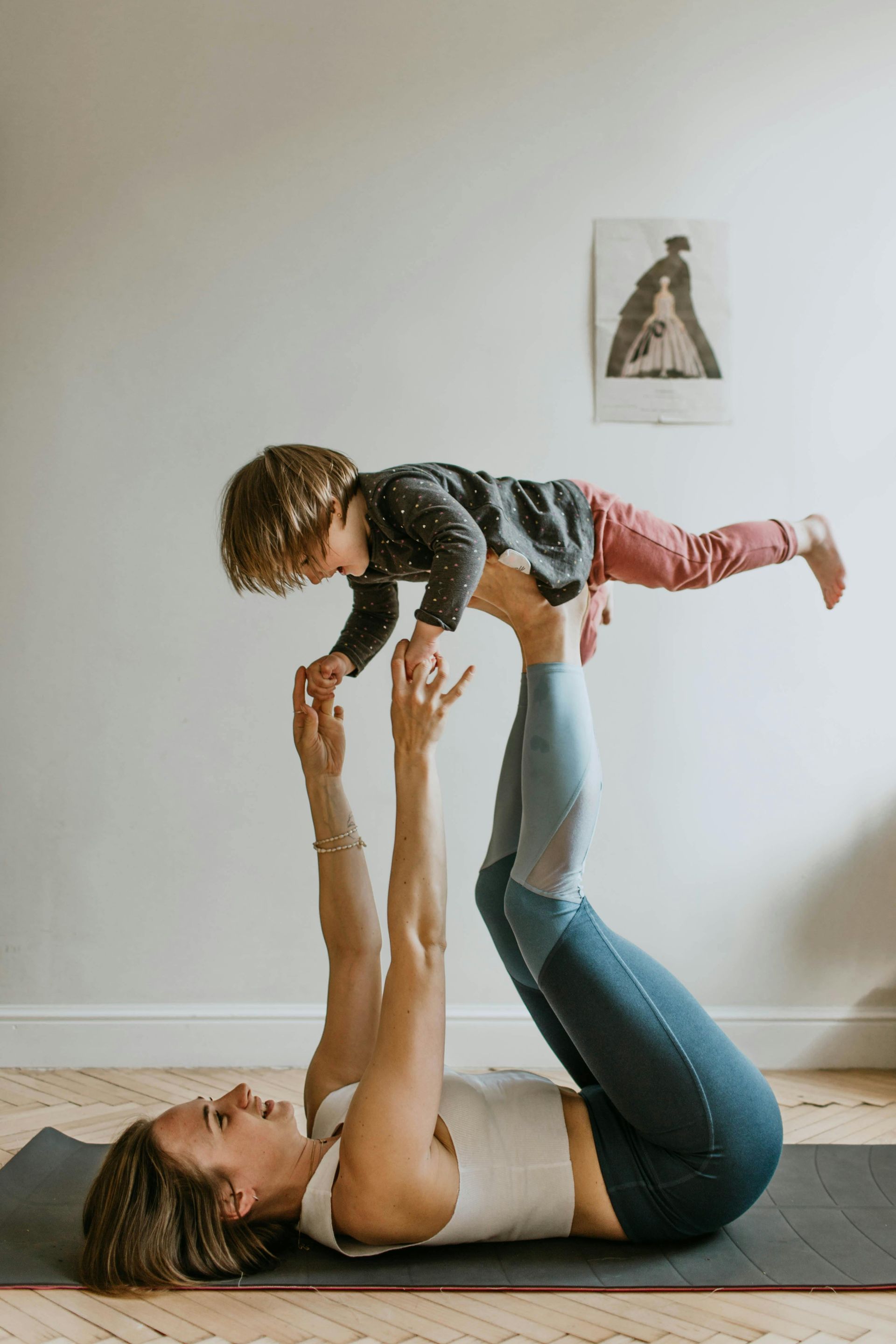 Woman doing acro yoga, lifting child with legs and hands on a yoga mat.