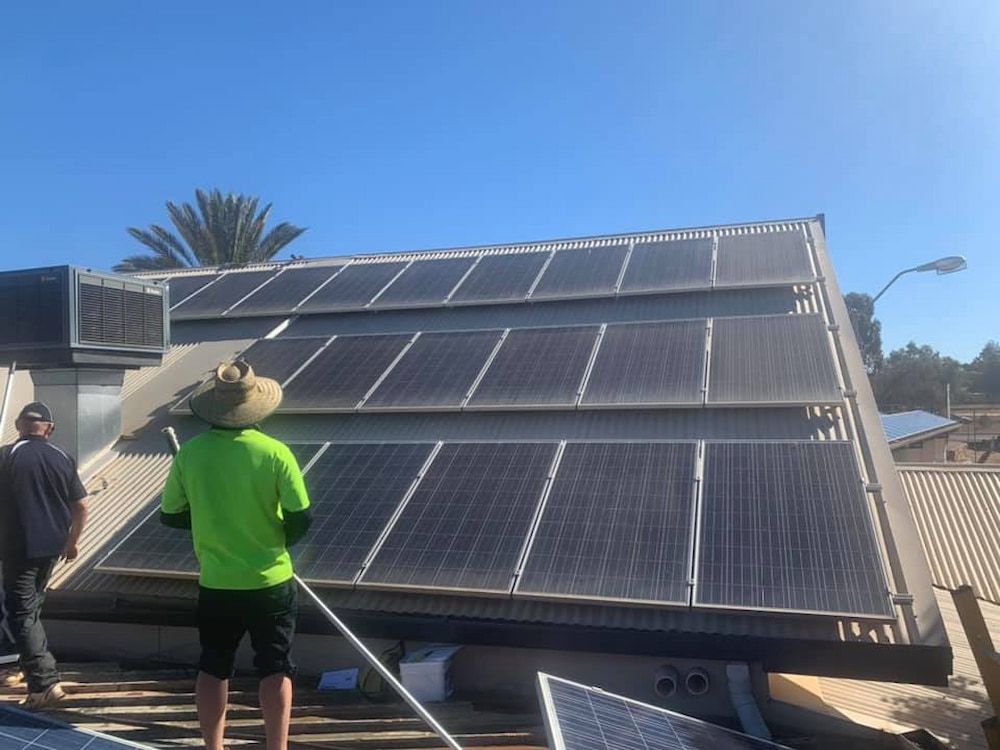 A man in a green shirt is standing on top of a roof with solar panels.— Tr!pl3 Fire Electrical & Contracting in Alice Springs, NT