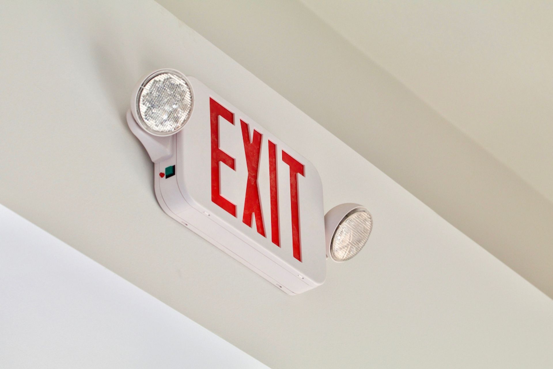 A Red and White Exit Sign With a Light Attached to It — Tr!pl3 Fire Electrical & Contracting in Alice Springs, NT
