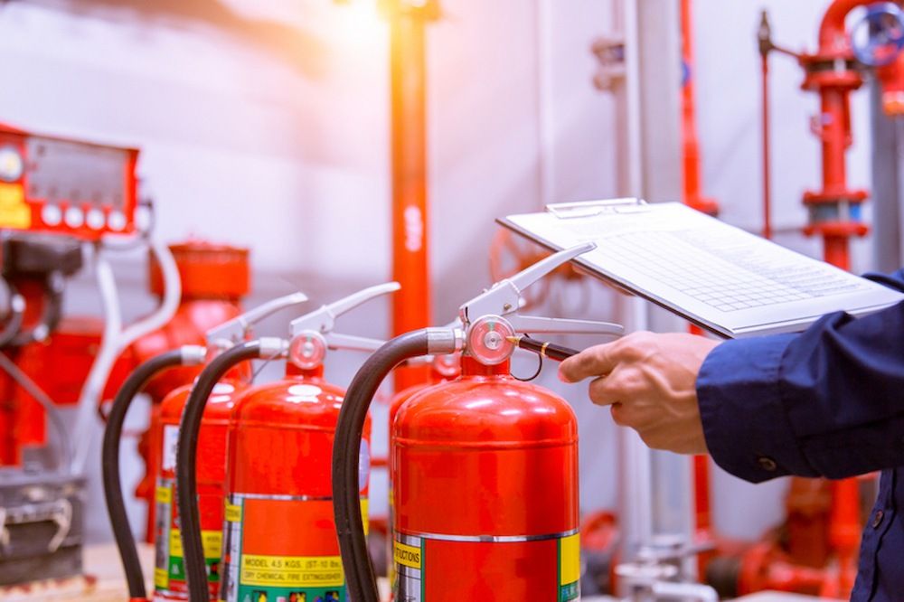 A Man Holding a Clipboard in Front of a Fire Extinguishers — Tr!pl3 Fire Electrical & Contracting in Alice Springs, NT