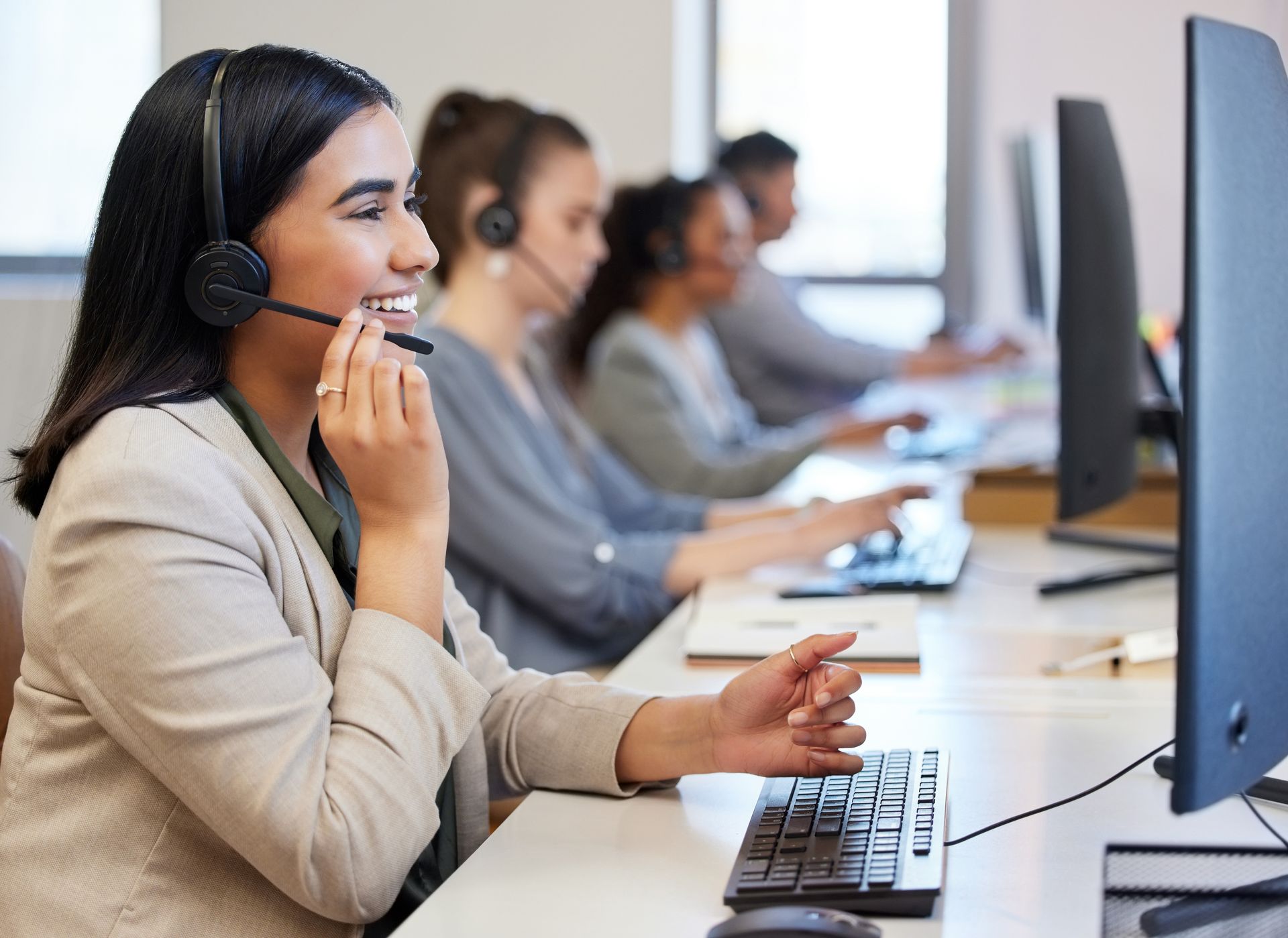 A woman wearing a headset is sitting in front of a computer in a call center.