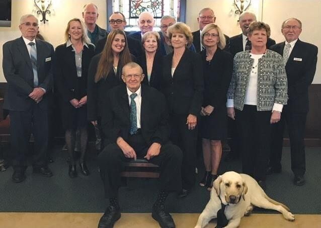 Group portrait in a formal room, with a seated man and a yellow Labrador in front.