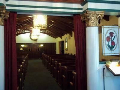 Church interior with pews, red curtains, and ornate white columns leading to the altar