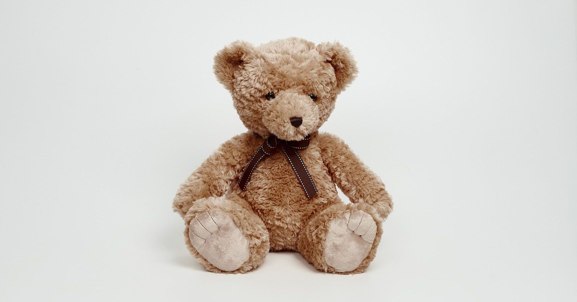 Brown teddy bear sitting on a white background with a small ribbon around its neck