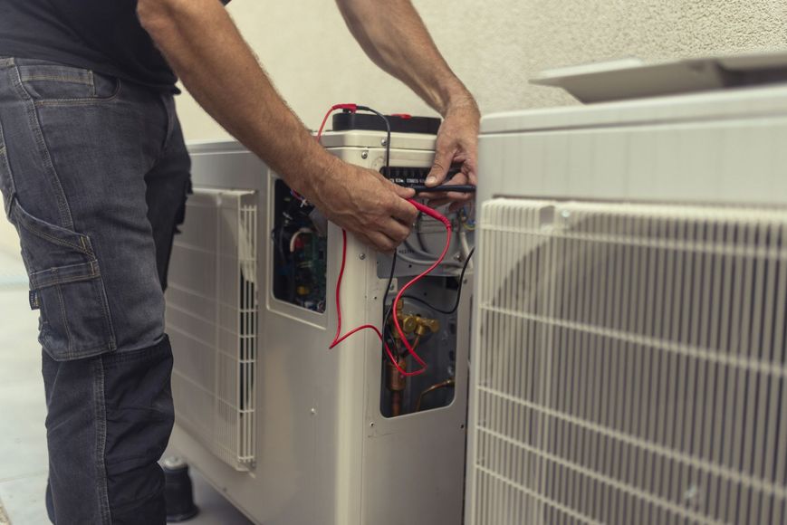 A man is working on an air conditioner outside of a building.