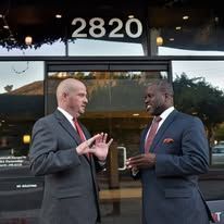 Two men in suits talking in front of a building with the address 