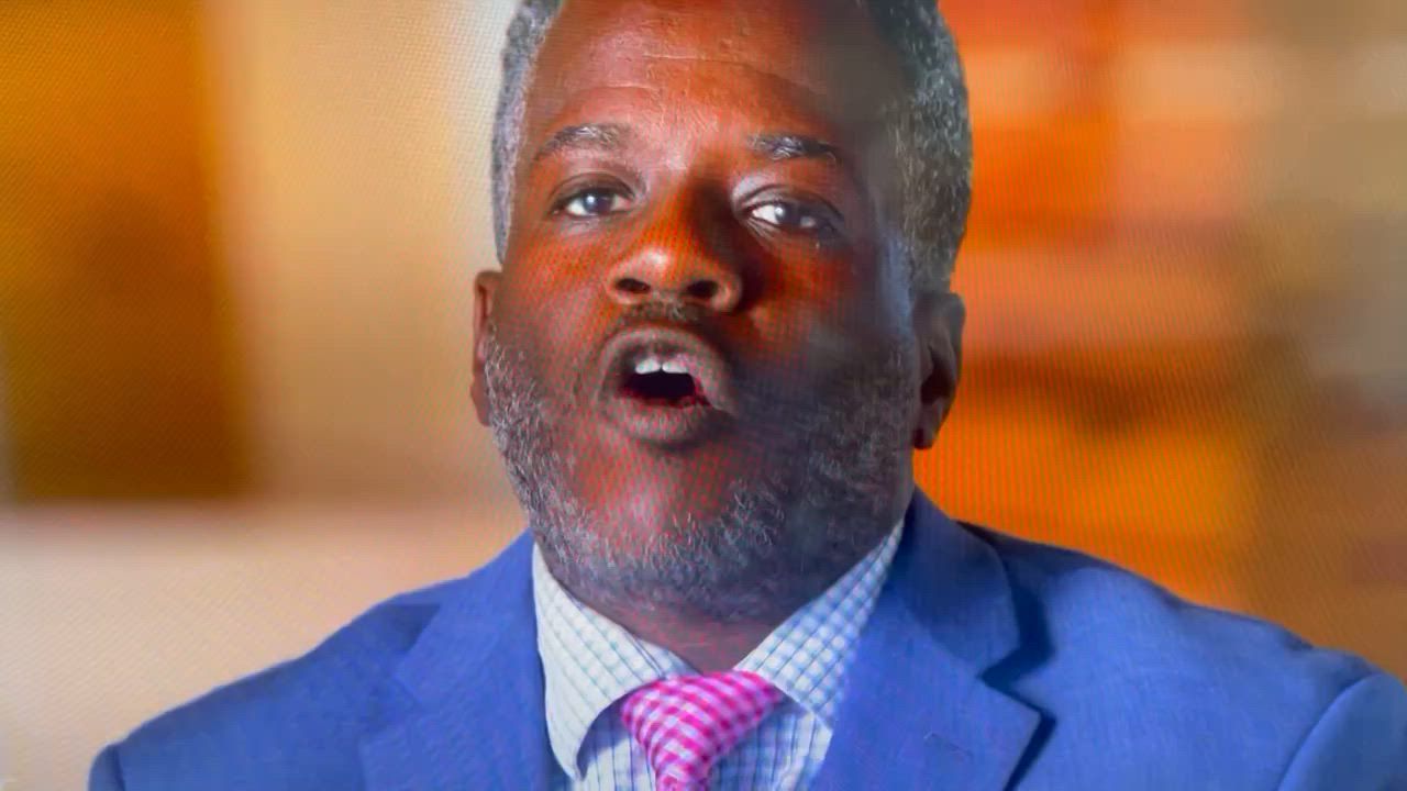 Man in blue blazer, open mouth, pink tie, surprised expression.
