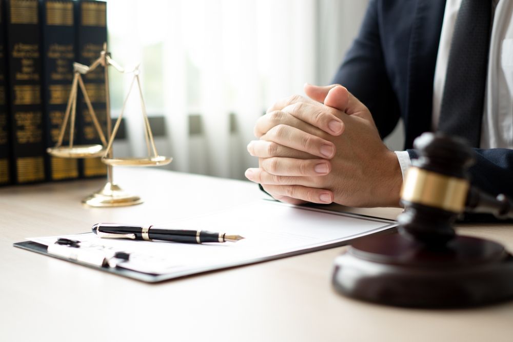 Scales of justice, gavel, and lawyer with folded hands at a desk.