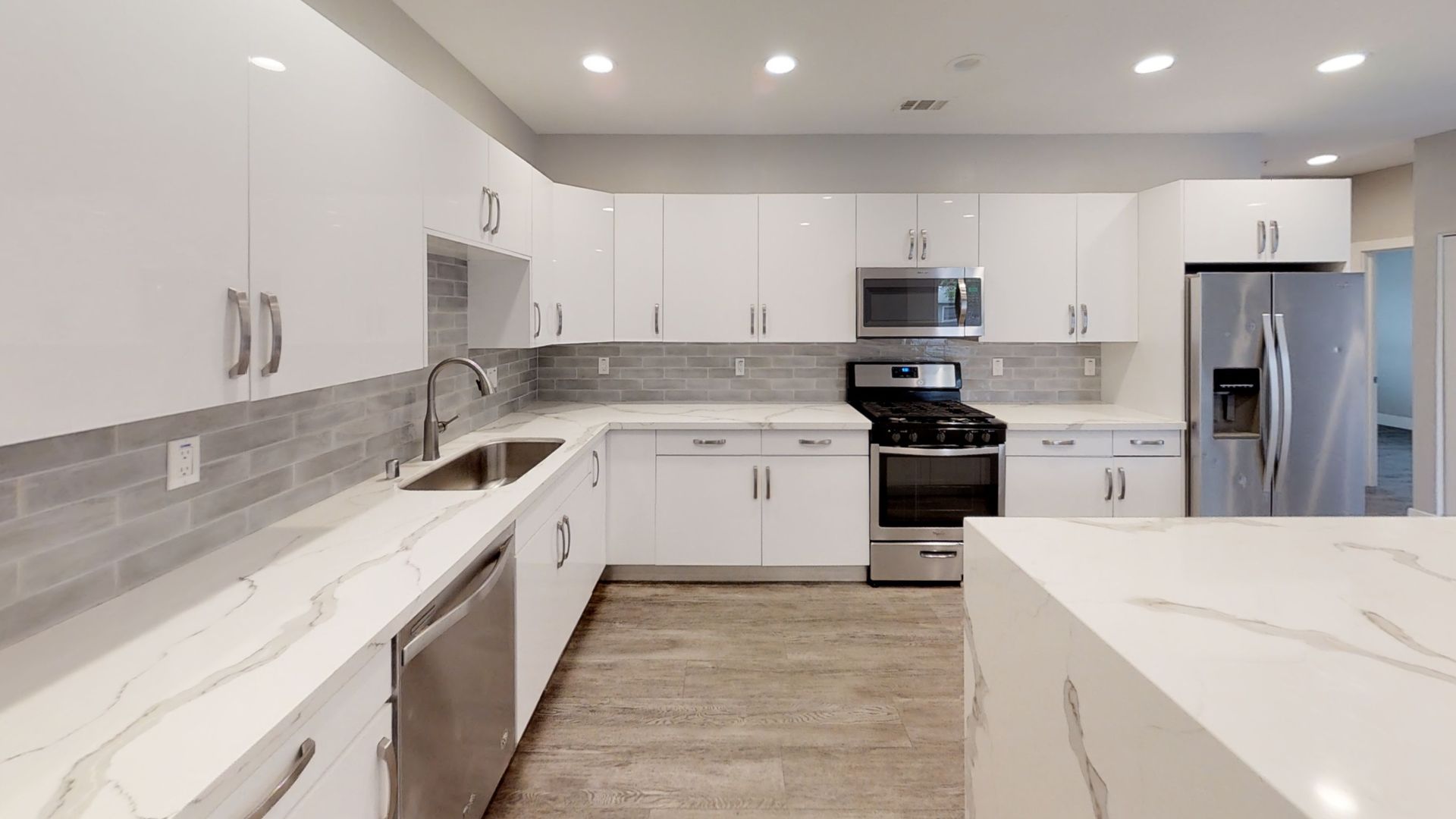 Modern white kitchen with stainless steel appliances, gray backsplash, and quartz countertops.