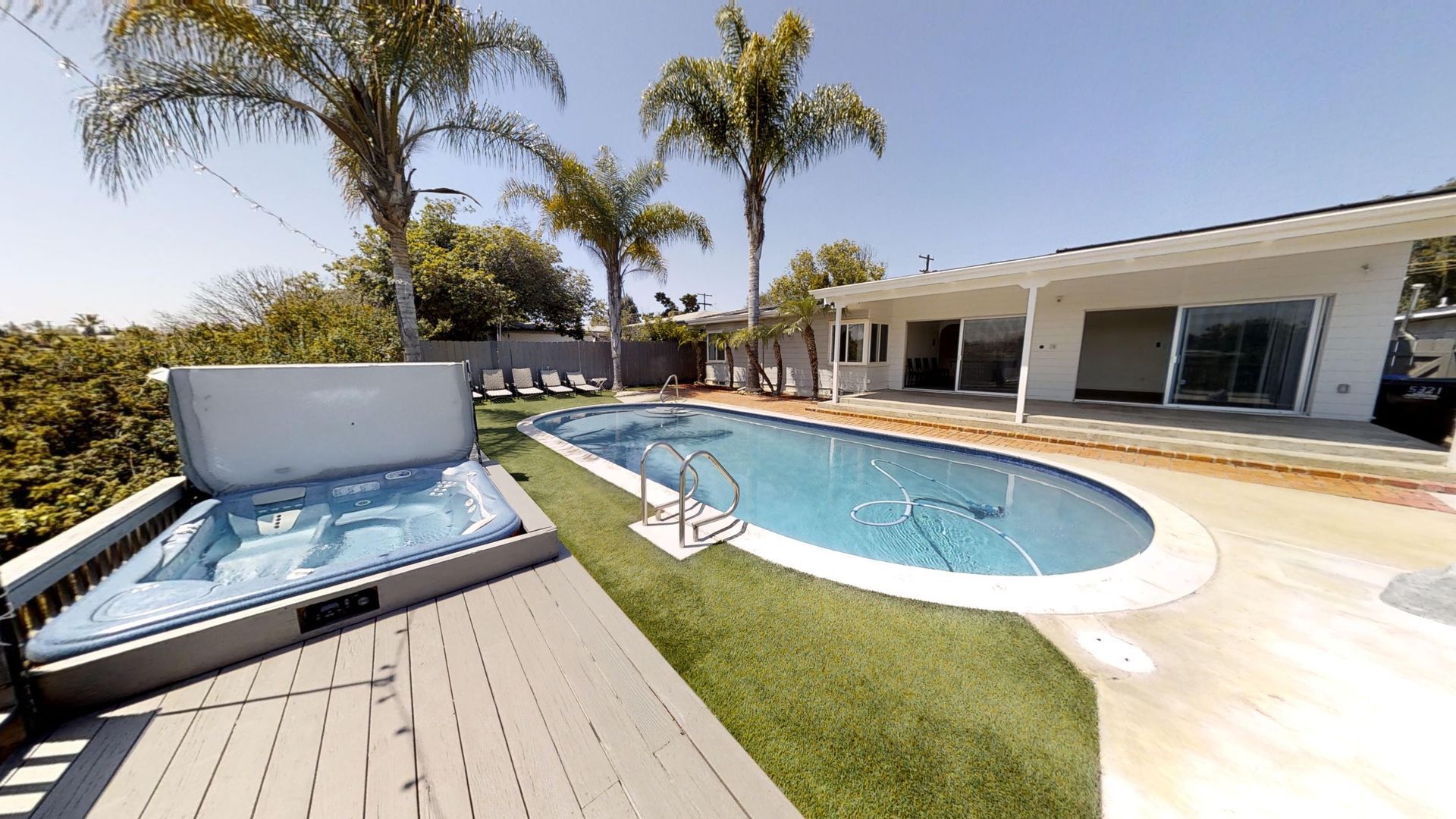 Backyard with pool, spa, and home. Palm trees and blue sky. Wooden deck and green turf.
