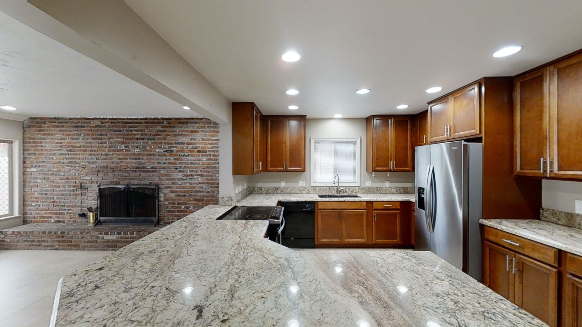 Kitchen with granite countertops, brown cabinets, and a brick fireplace.