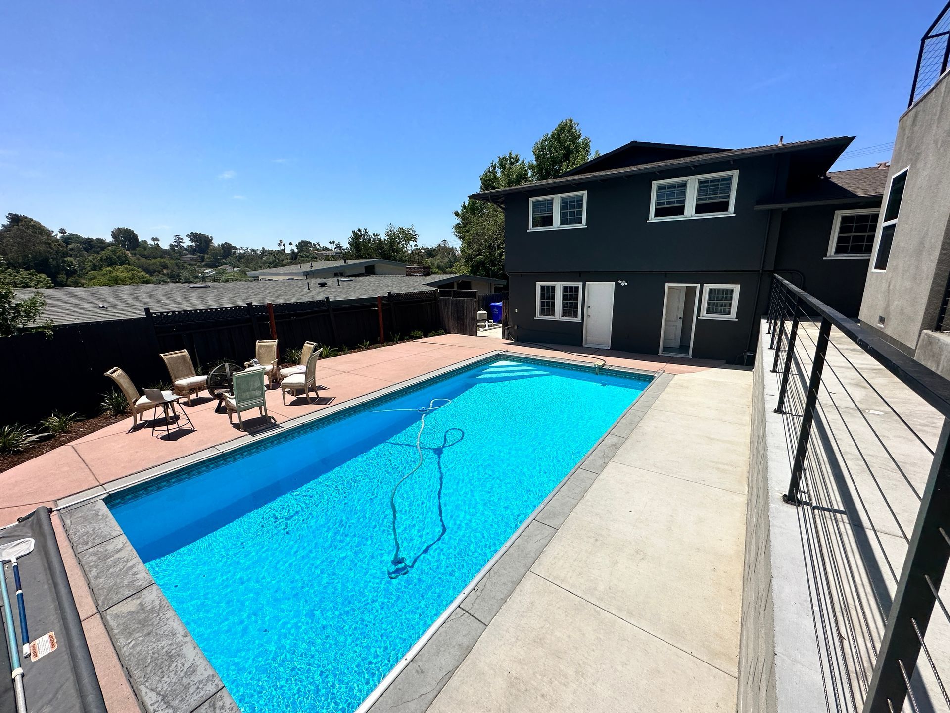A backyard with a pool, lounge chairs, and a two-story dark house on a sunny day.