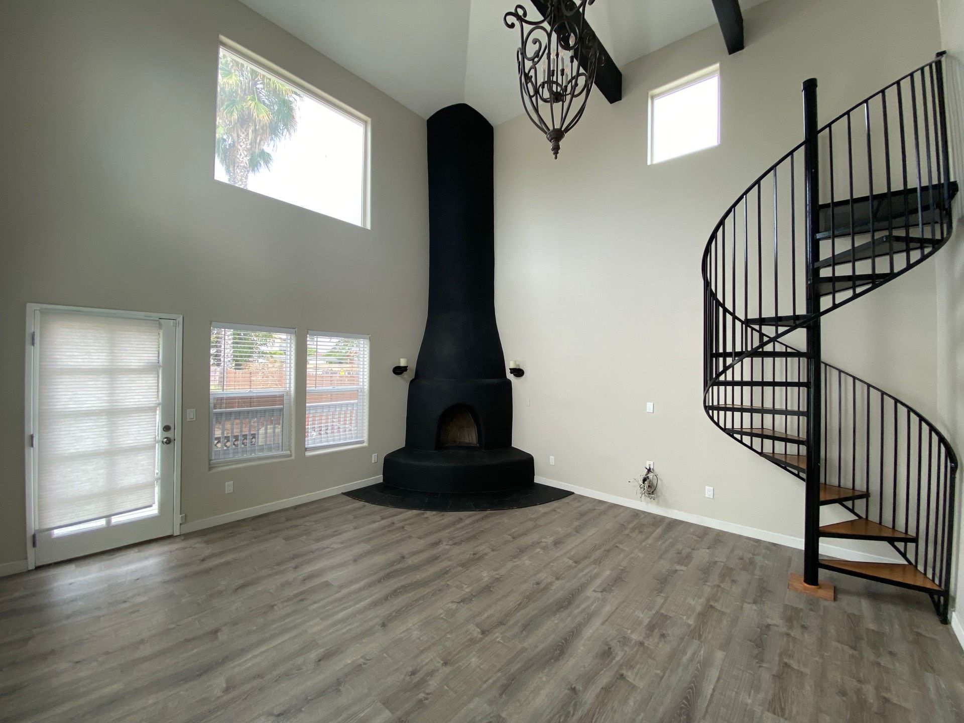An empty room with a black spiral staircase, fireplace, and large windows.