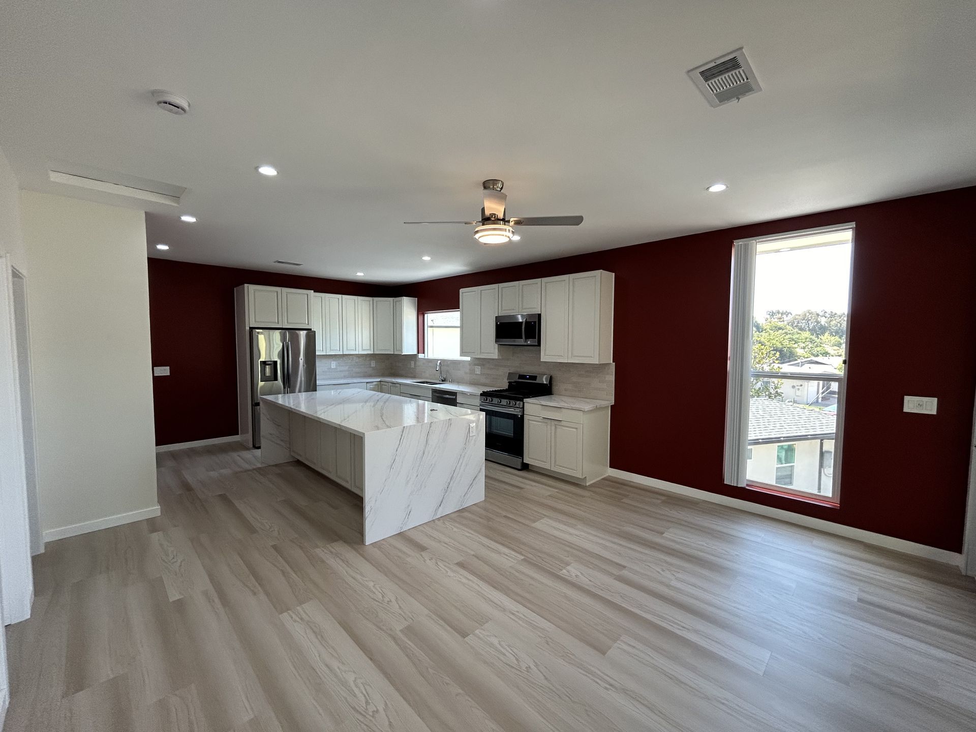 Modern kitchen with white cabinets, marble island, red walls, and light wood floors.