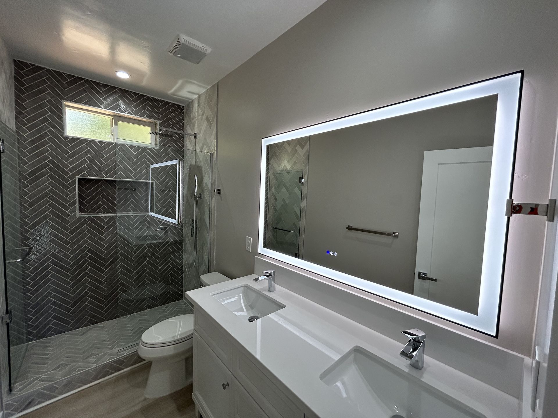 Modern bathroom with dual vanity, lighted mirror, and tiled shower.