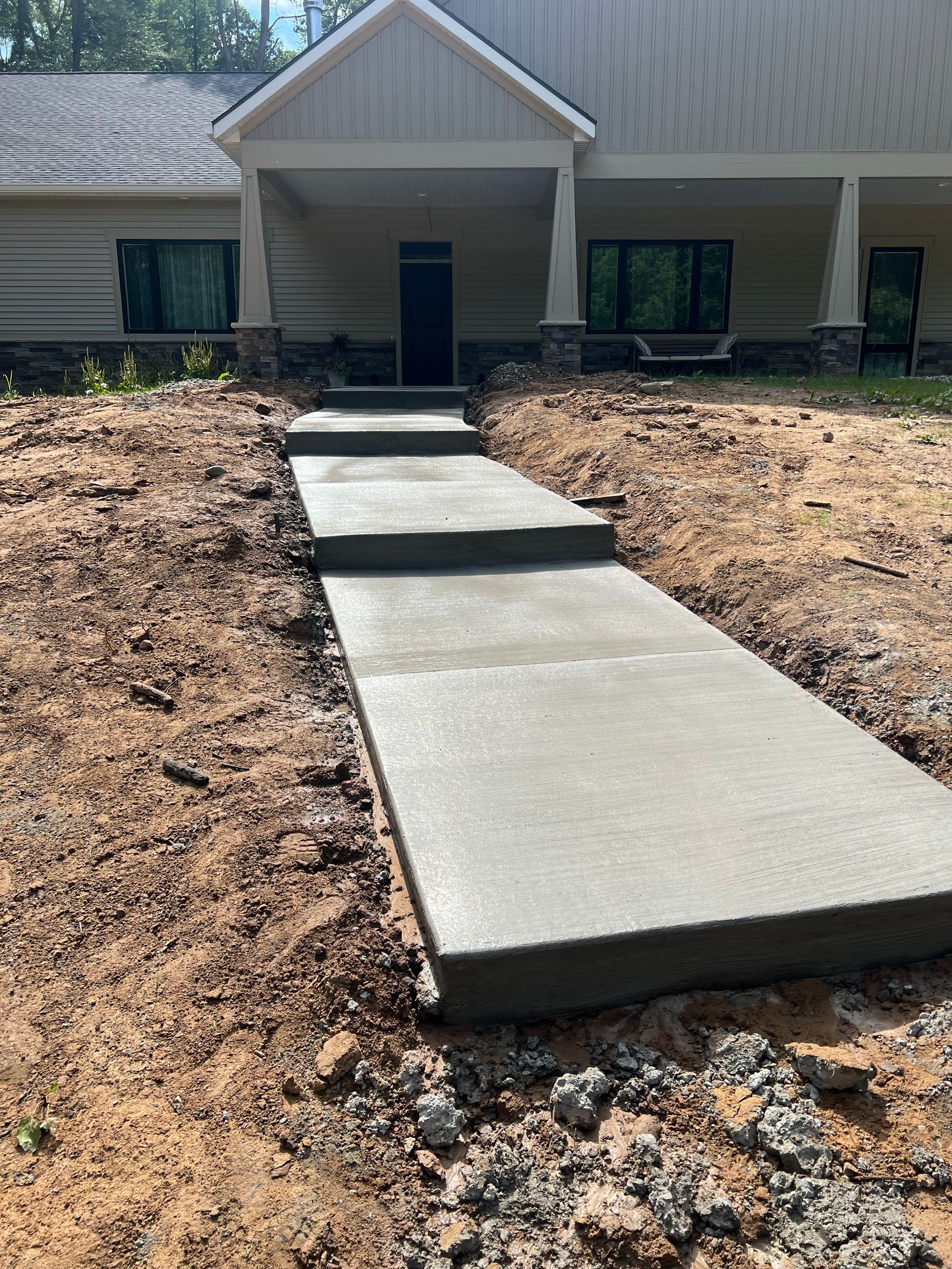 Concrete walkway and steps leading to a house entrance; dirt surrounding.