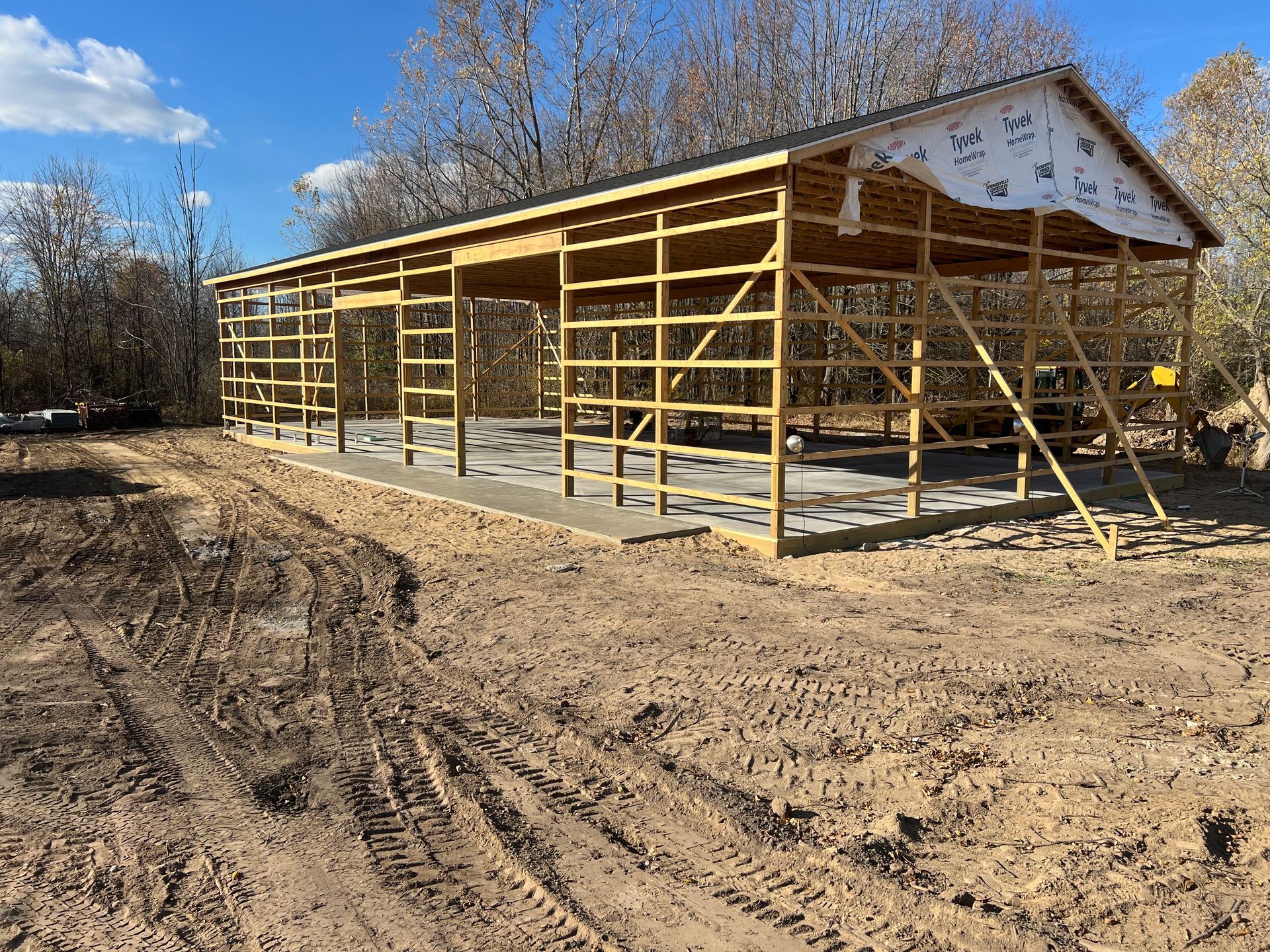 Wooden frame of a barn under construction on a dirt lot; blue sky in the background.