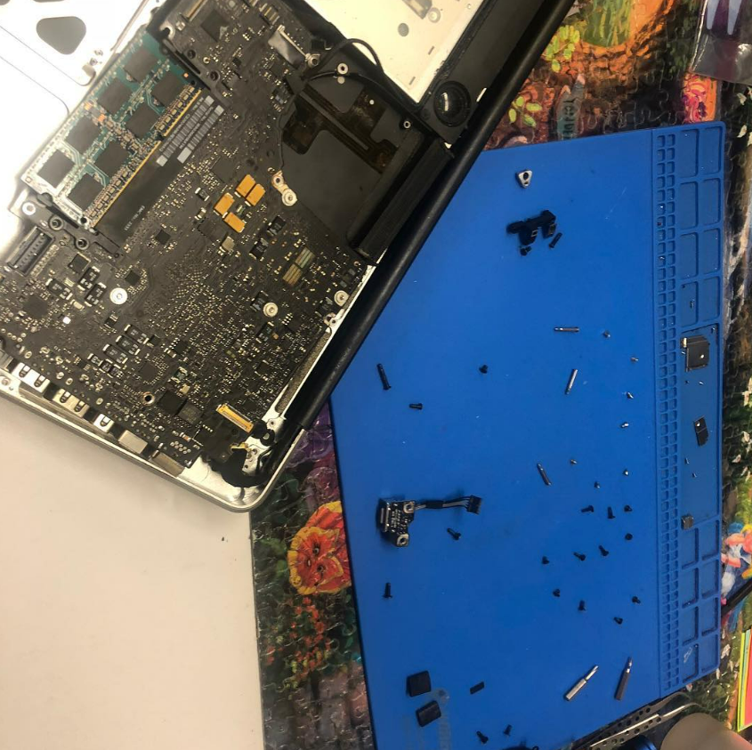 Disassembled laptop with exposed circuit board beside a blue plastic back cover and loose screws.