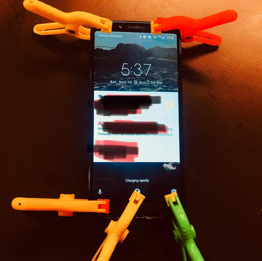 Smartphone on dark surface surrounded by orange and green clothespins, screen showing 5:37 and app notifications