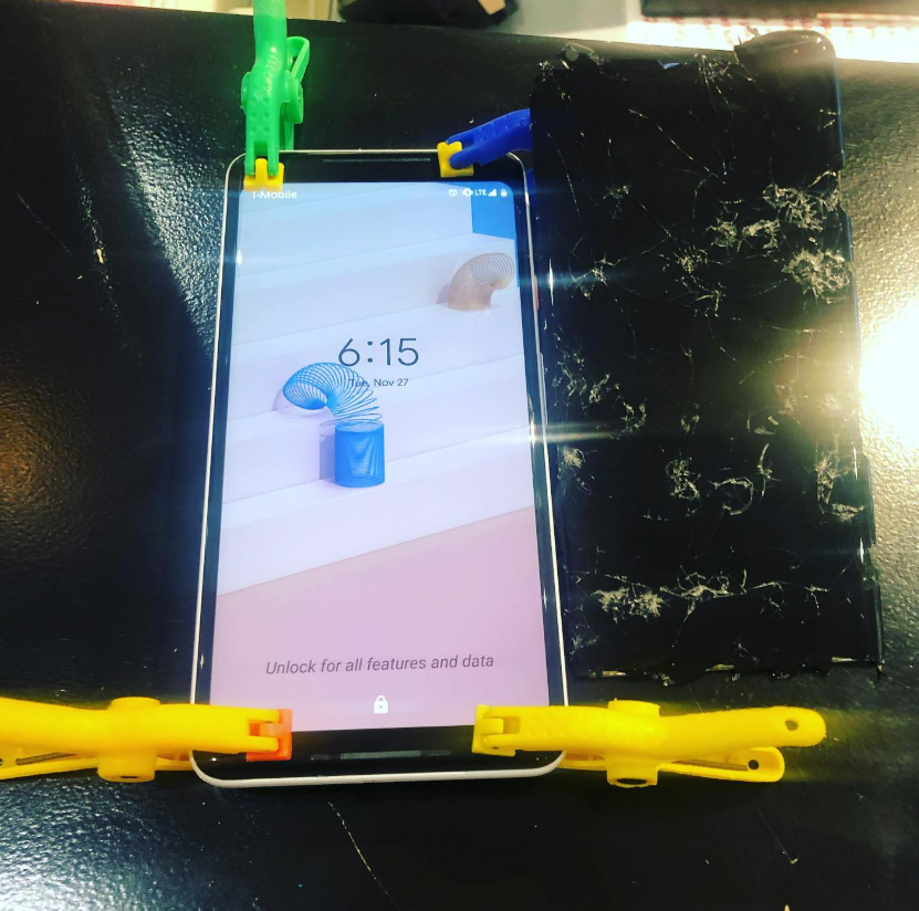 Smartphone screen clamped in a black rig with colorful clips, showing a lock screen at 6:15.