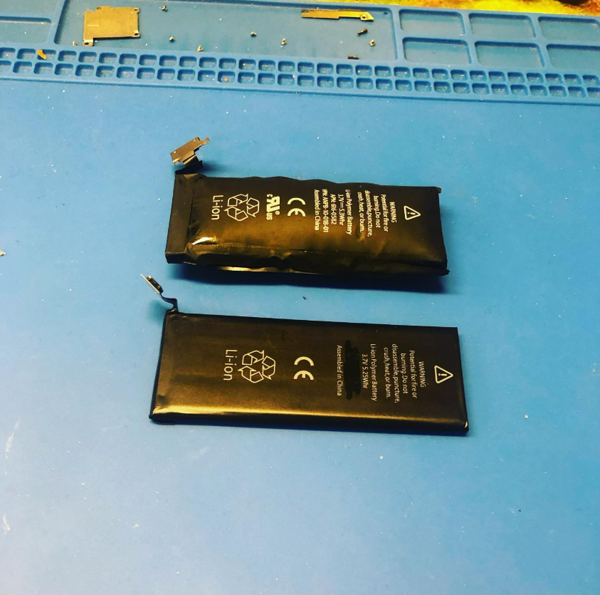 Two black lithium battery pouches on a blue work mat, one torn open with a loose tab.