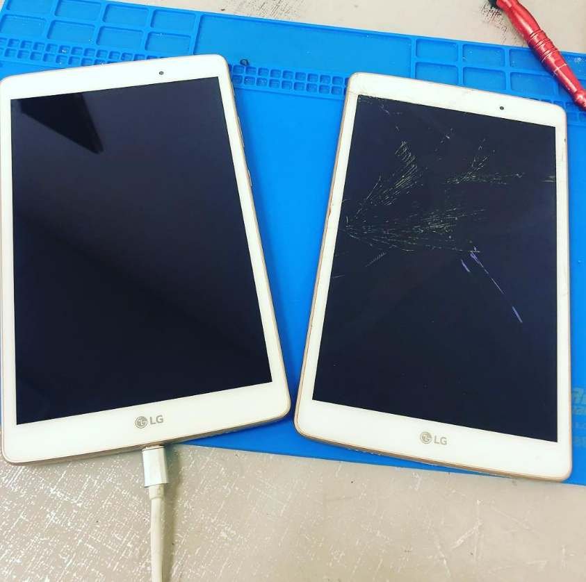 Two damaged white LG tablets on a blue mat, one with a charging cable attached.