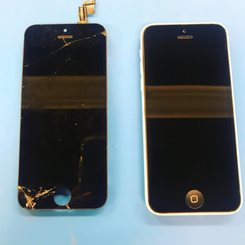 Two cracked black smartphones side by side on a light blue surface, one with a broken top and bottom screen.