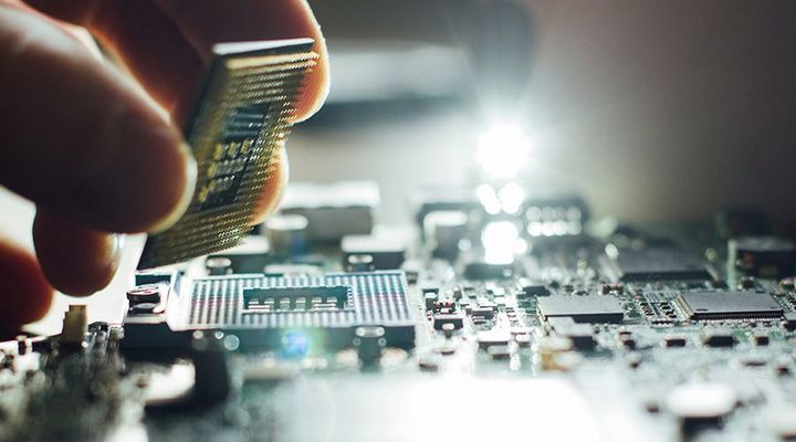 Hand placing a microchip on a circuit board with components in a bright close-up shot