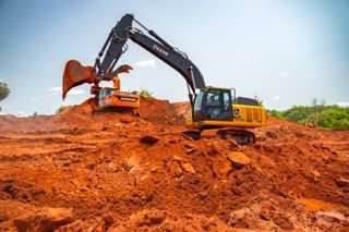 Excavator digging red dirt on a construction site under a blue sky