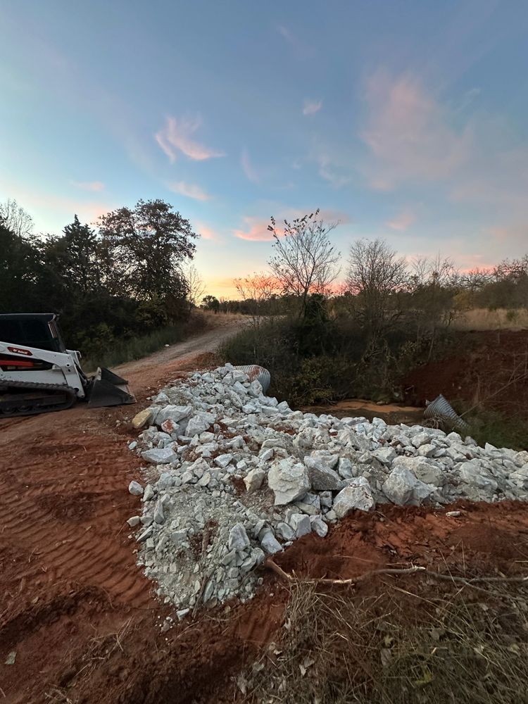 Rural dirt road at sunset with a white stone barrier and a partially visible parked vehicle on the left