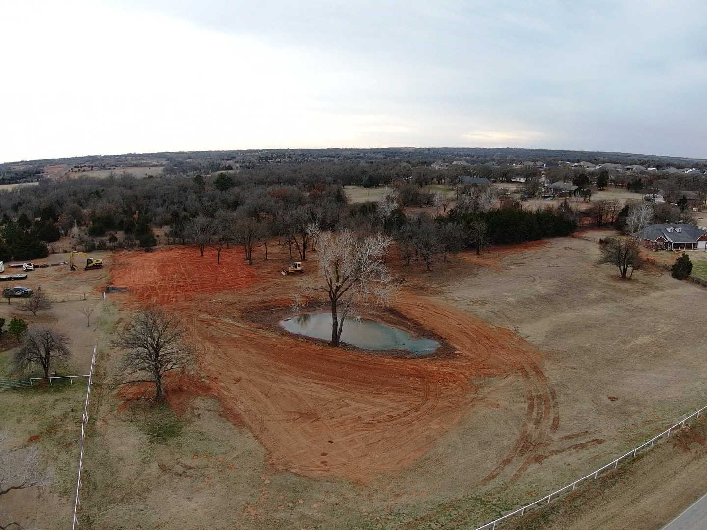 Aerial view of a rural landscape with a pond, orange construction soil, and scattered trees.