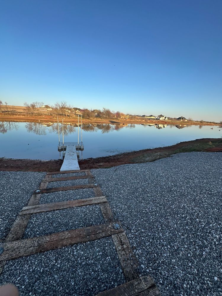 Wooden dock extends into a calm lake at sunrise, with a clear blue sky and shoreline reflections.