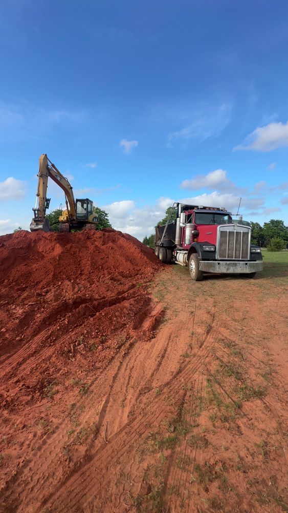 Excavator and red dump truck on a dirt construction site under a blue sky