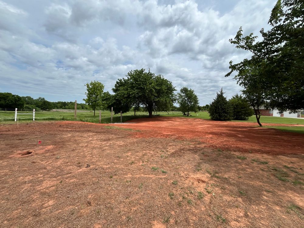 Red dirt clearing with scattered trees under a cloudy sky.
