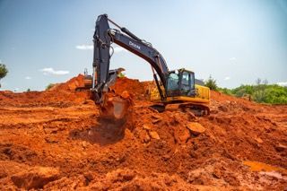 Excavator digging red soil on a construction site under a clear sky