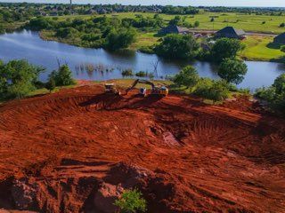 Red earth construction site beside a winding river with green fields and trees in the background