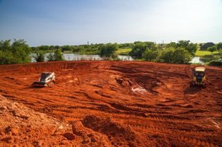 Red dirt construction site with two small vehicles and trees in the background