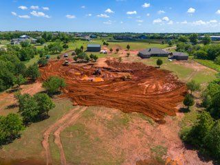 Aerial view of a muddy red construction site with machinery and houses in the distance