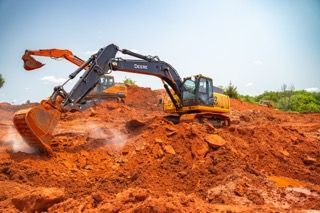 Excavator digging red soil at a construction site under a clear sky
